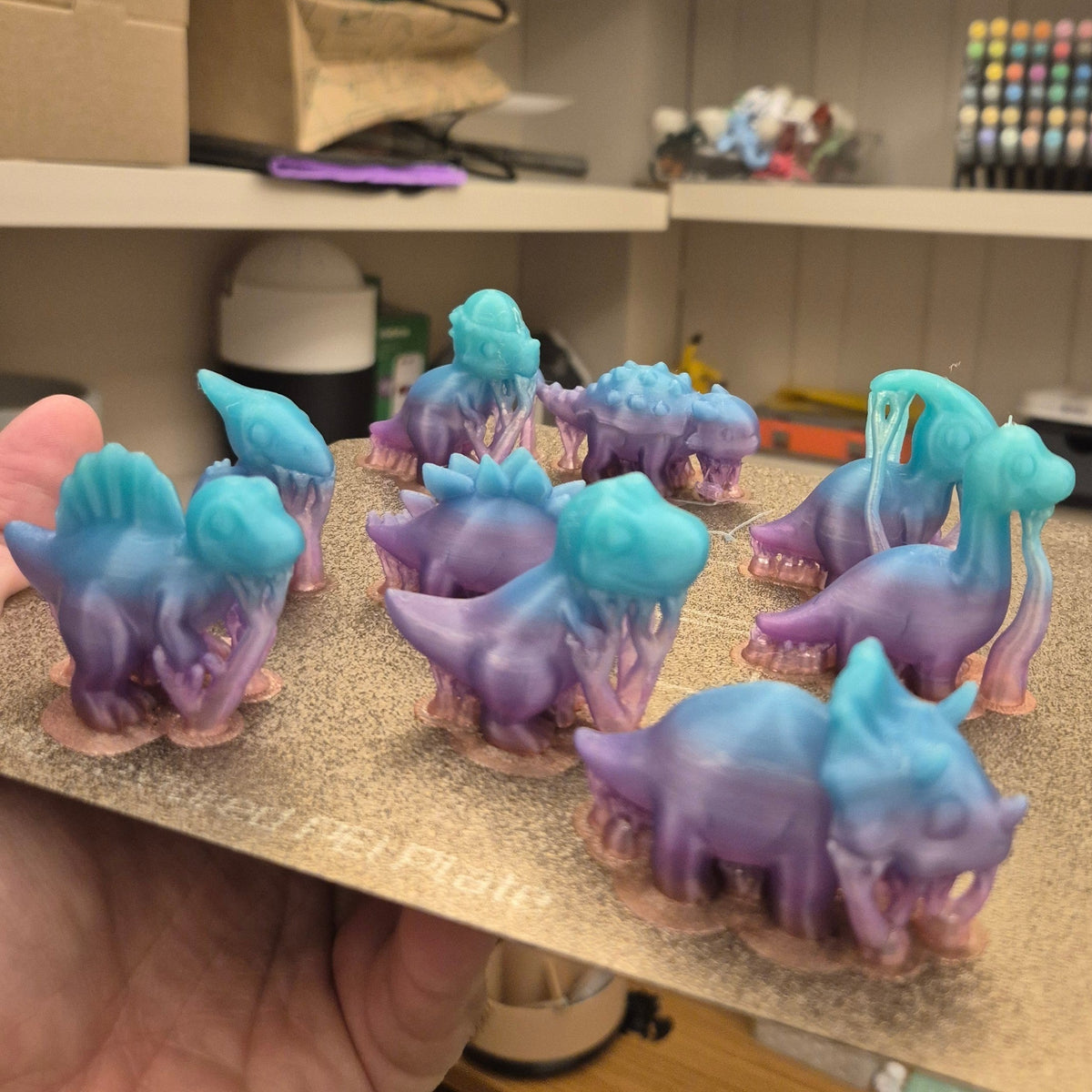 Kit de 11 mini dinossauros Minha loja em tons degradê de azul e roxo, impressos em resina sobre base de suporte.