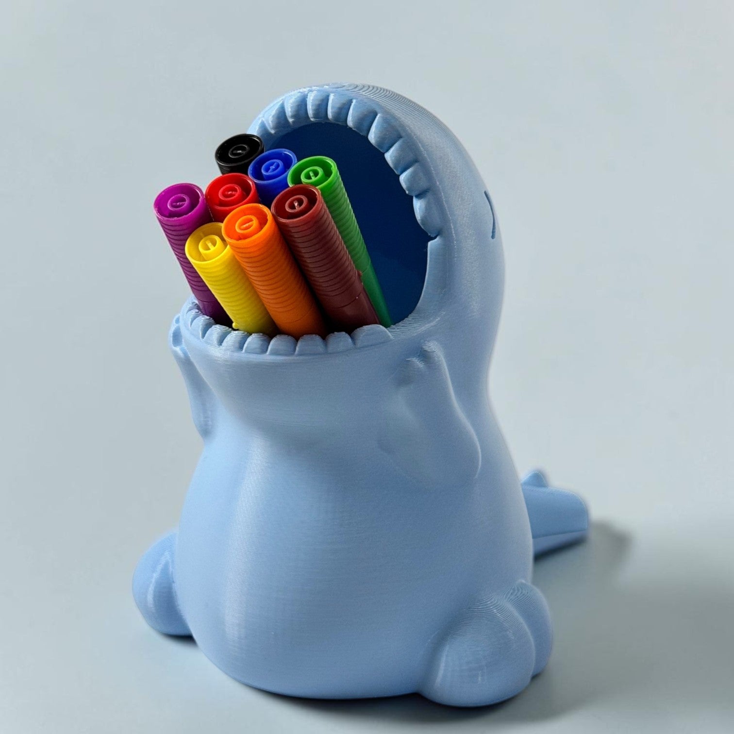 Porta-lápis Minha loja em formato de dinossauro azul claro com canetinhas coloridas para organização infantil