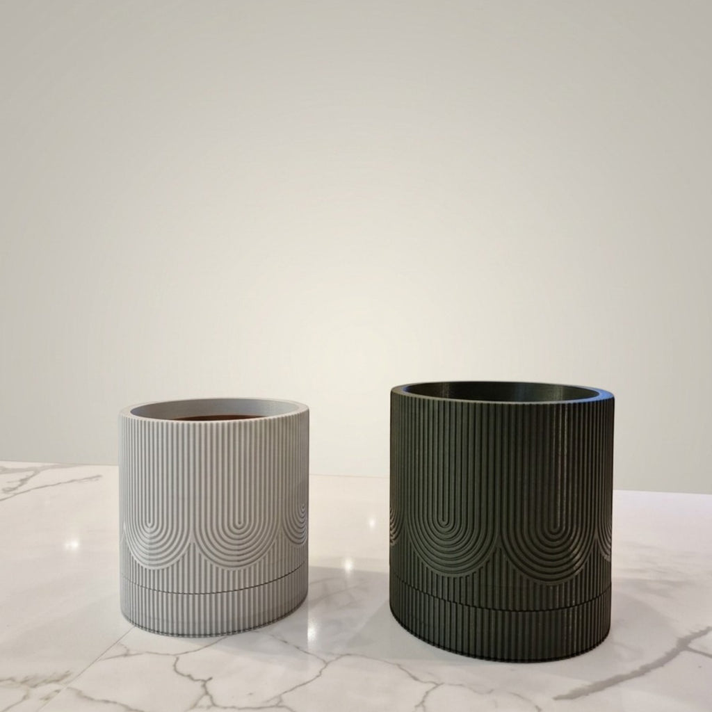 Vasos Minha loja cilíndricos com bandeja coletora, texturizados em cinza claro e verde escuro sobre mesa de mármore.