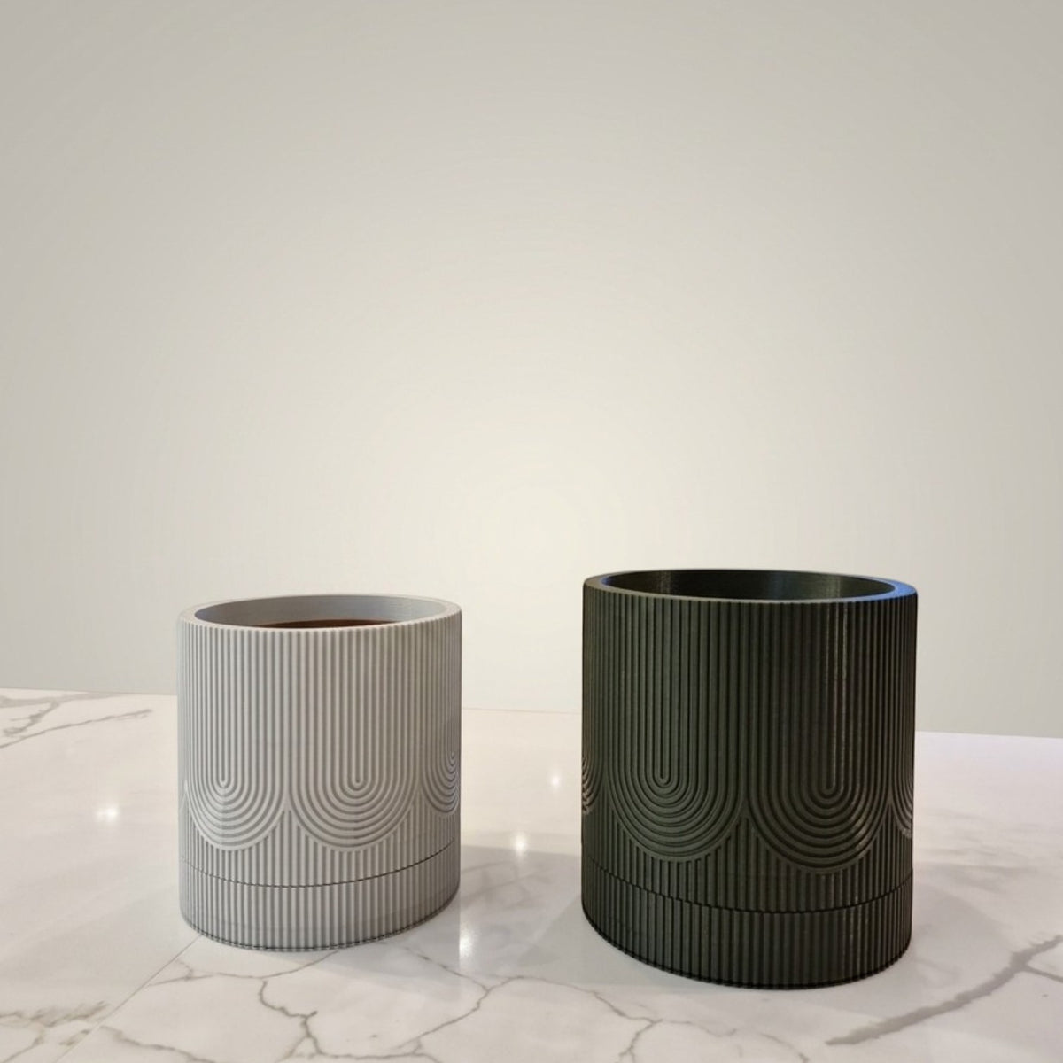 Vasos Minha loja cilíndricos com bandeja coletora, texturizados em cinza claro e verde escuro sobre mesa de mármore.